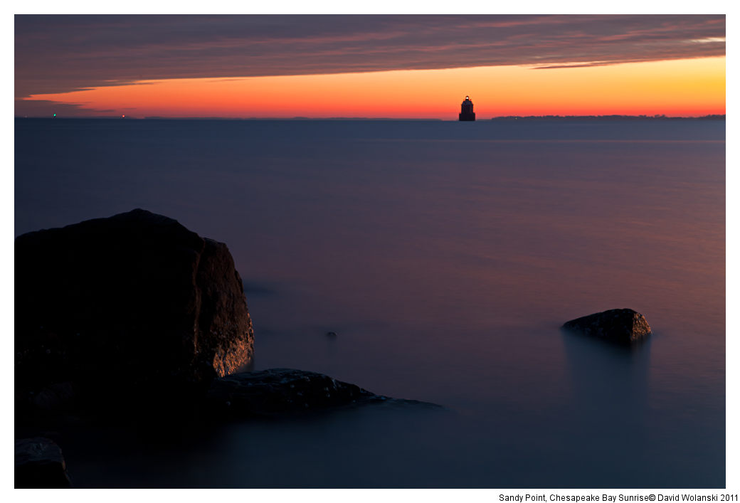 Morning light glows on rocks, with smooth water from long exposure and lighthouse in the back