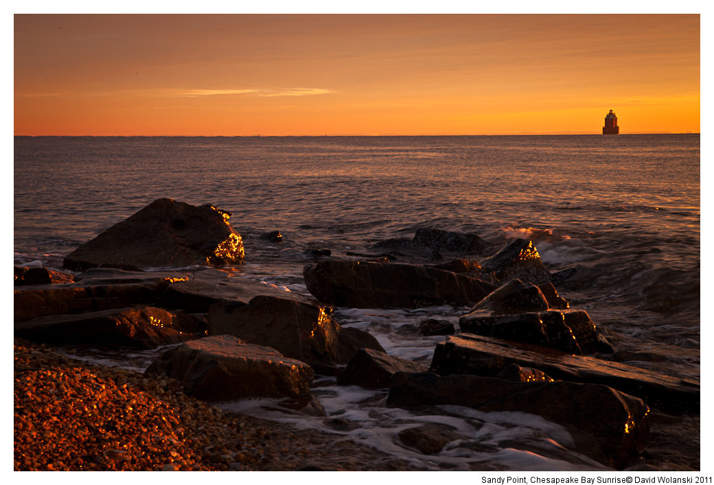 Golden hour sunlight glinting off the rocks, Sandy Point Light House behind it